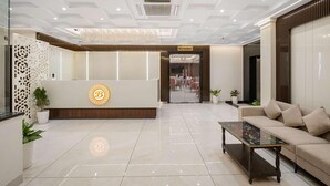 Zona de recepción de un hotel con diseño moderno, que incluye un mostrador de recepción, un área de descanso y una escalera que lleva al restaurante.
