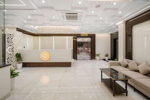 A hotel reception area with a modern design, including a reception desk, seating area, and a staircase leading to the restaurant. - Hotel The Balram (Ayodhya)