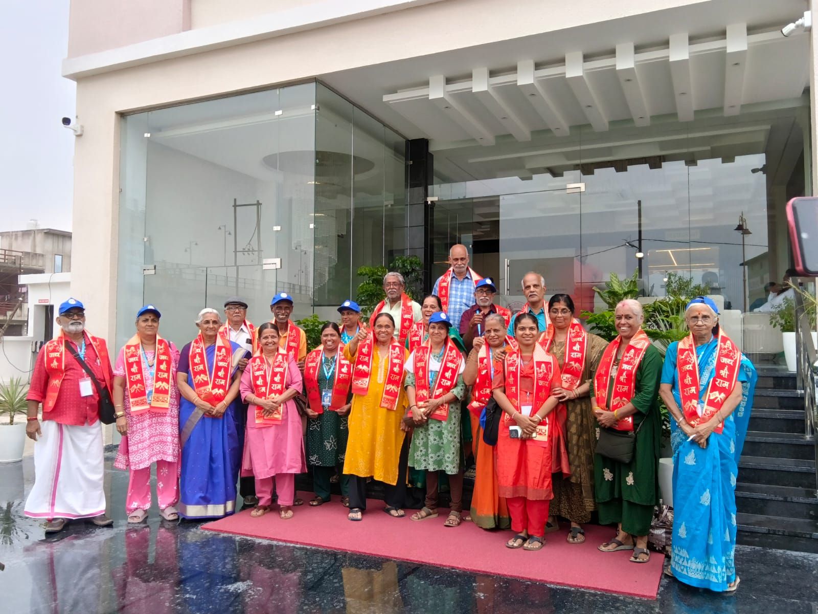 Un grupo de personas de pie sobre una alfombra roja frente a un edificio moderno con puertas de vidrio.