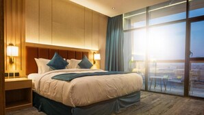 Ein Hotelzimmer mit einem großen Bett, einem Nachttisch, einem Fenster mit Blick und einem Holzkopfteil.