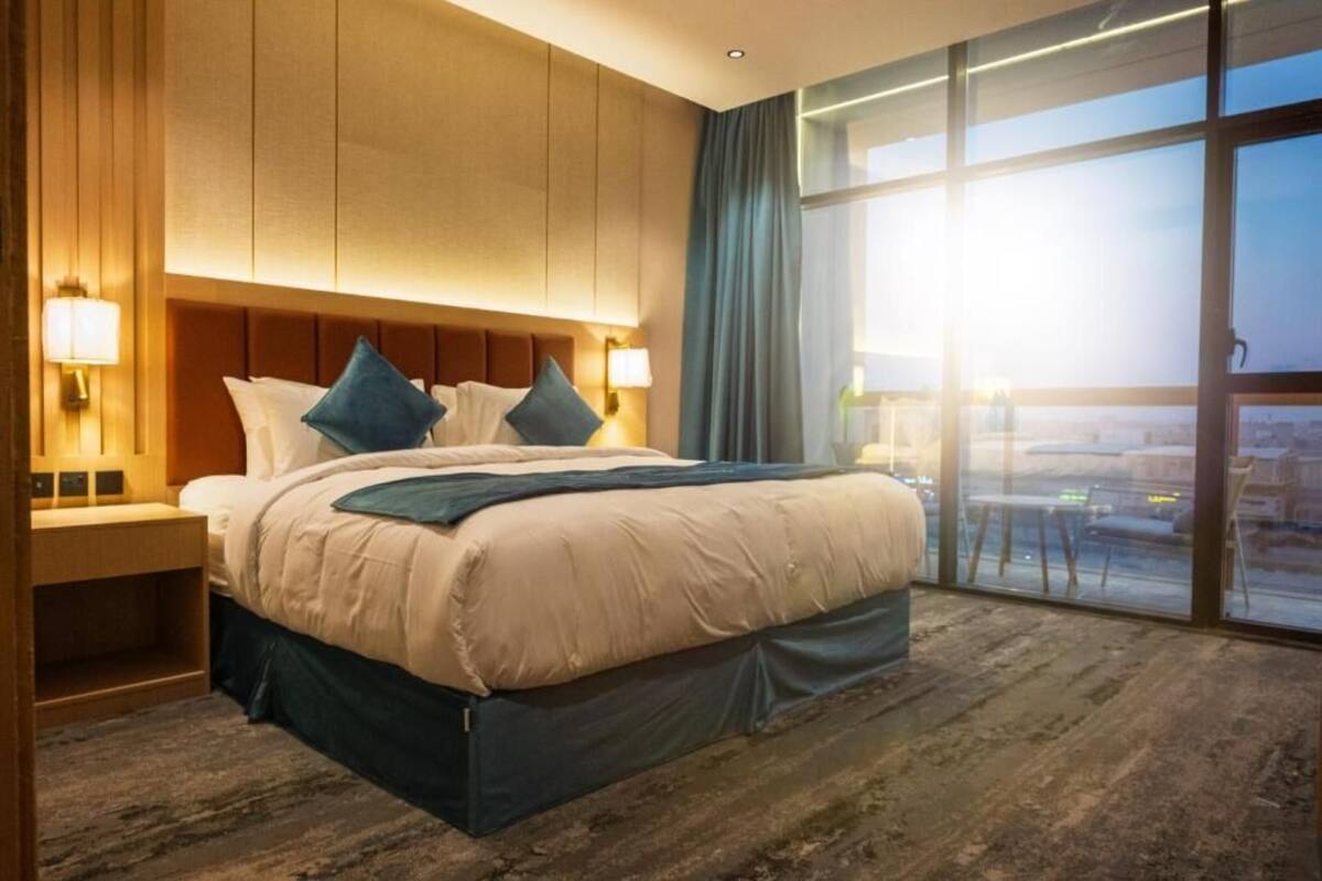 A hotel room with a large bed, a nightstand, a window with a view, and a wooden headboard.