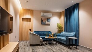 Ein modernes Hotelzimmer mit einer Couch, einem kleinen runden Tisch, einem Fernseher und einer Klimaanlage.