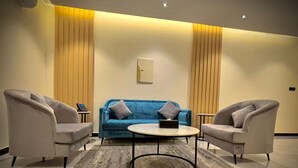 Ein moderner Lounge-Bereich mit einem blauen Sofa, zwei Sesseln, einem Couchtisch und einem gemusterten Teppich.