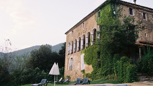 A pool with lounge chairs and umbrellas, a stone building with arches, and a mountainous backdrop. - Casa Rural Mas Garganta (La Vall d'en Bas)