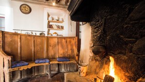 A cozy room with a stone fireplace, wooden benches, and shelves with books and decorative items. - Casa Rural Mas Garganta (La Vall d'en Bas)