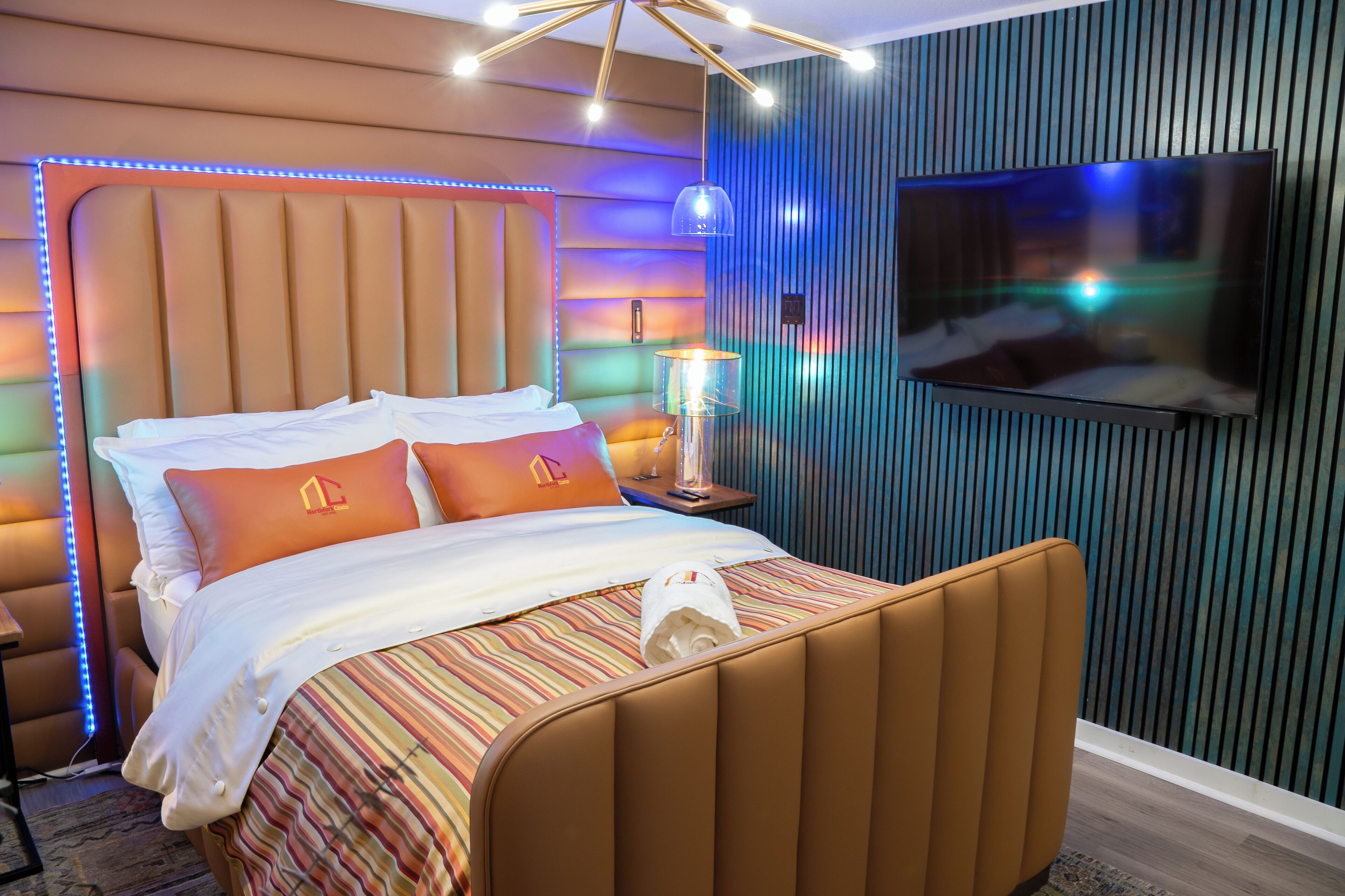 Ett modernt hotellrum med en stor säng, en tv som är monterad på väggen och stämningsfull belysning.