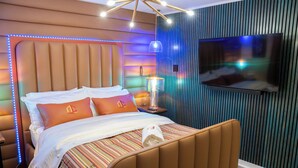 Una habitación de hotel moderna con una cama grande, un televisor montado en la pared e iluminación ambiental.
