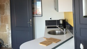 Une cuisine compacte dotée d’un plan de travail blanc, d’un évier en acier inoxydable et de deux suspensions industrielles.