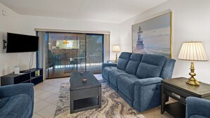 A modern living room with a sofa, coffee table, and lamps. There is a TV mounted on the wall and a painting on the wall.
