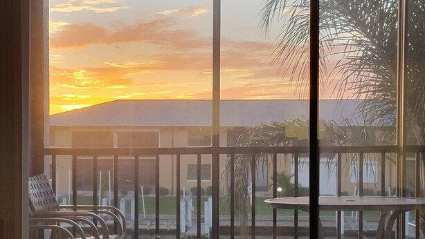 A balcony with a view of a sunset, a table, and chairs.