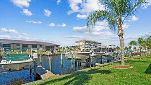 A marina with boats docked, a building with a flat roof, and a palm tree.