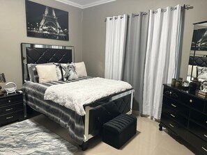A modern bedroom with a bed, bedside tables, a dresser, and a large window with curtains. - Elegant One Bedroom Luxury Apartment Overlooking Kingston (Kingston)