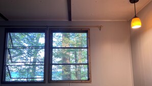 A room with a round table, two chairs, a window with a view of trees, and a hanging light fixture.