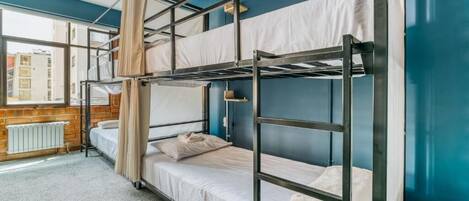 Habitación con literas y vista a edificios, un radiador y una lámpara colgante.