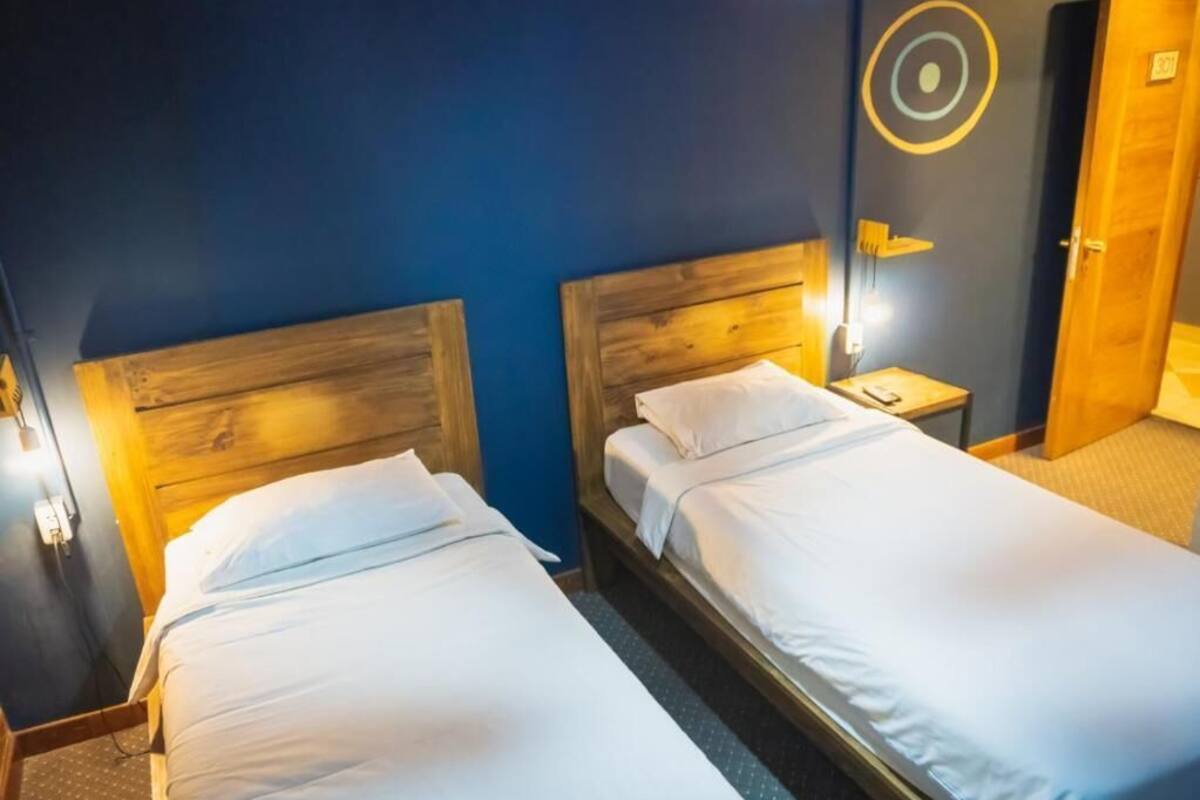 Two single beds with wooden headboards in a room with dark blue walls and a circular wall decoration.