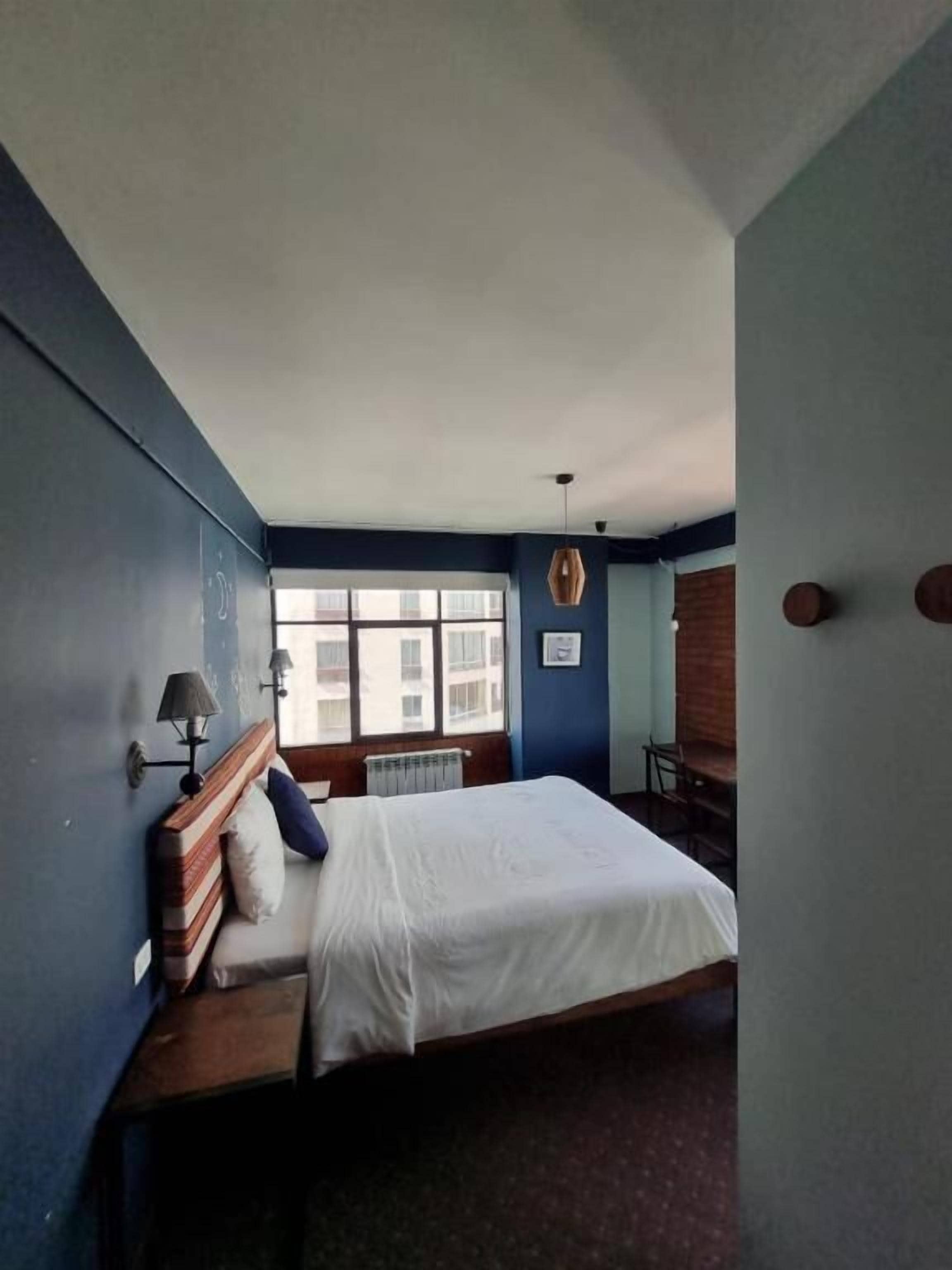 A bedroom with a bed, bedside lamps, a window, and a radiator.