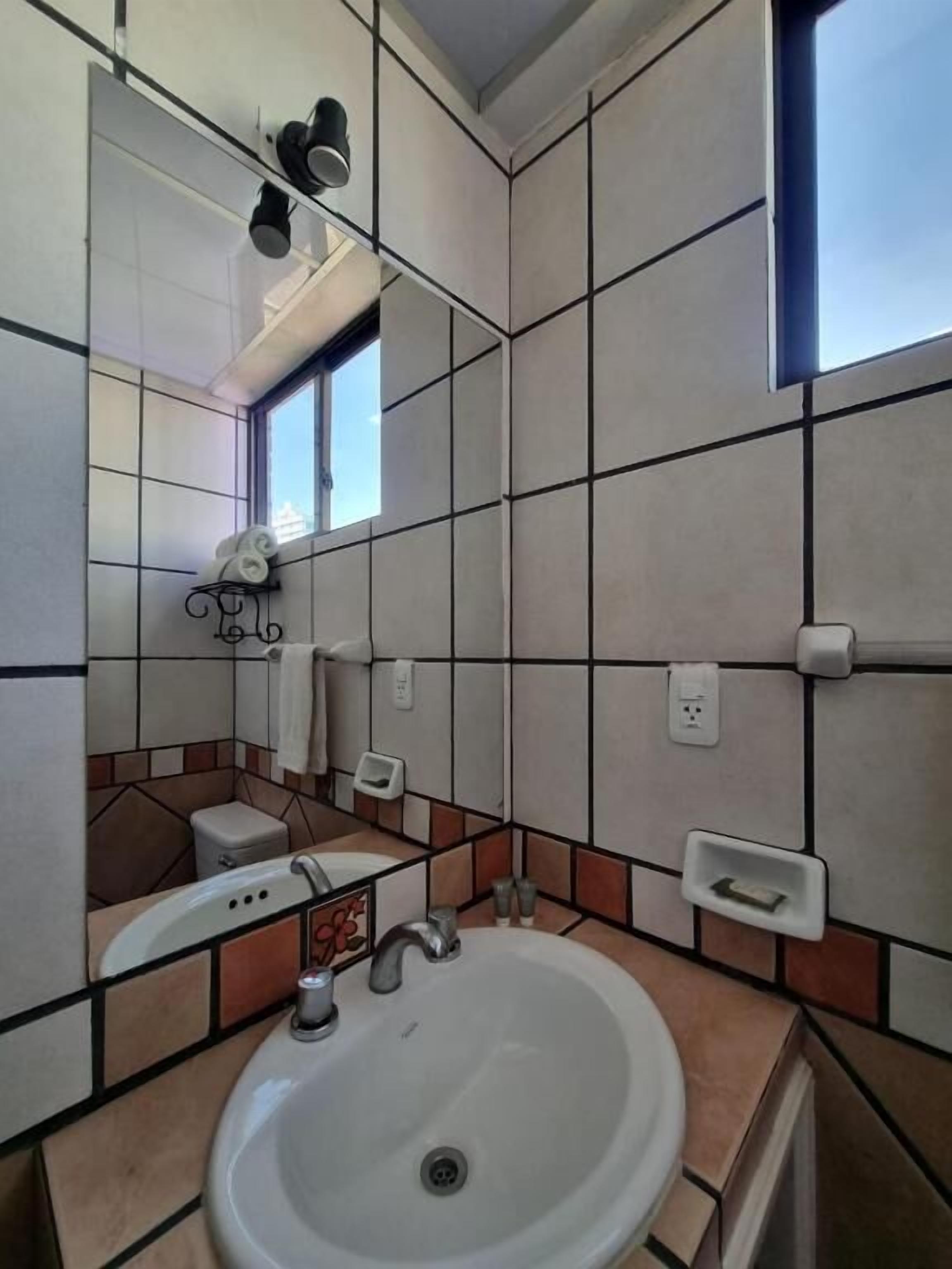 Une salle de bain avec un lavabo blanc, un miroir, un porte-serviettes et une fenêtre.