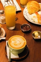 Ein Frühstückstisch mit Speisen, Orangensaft, einer Kaffeetasse mit Latte-Art und Gewürzen.