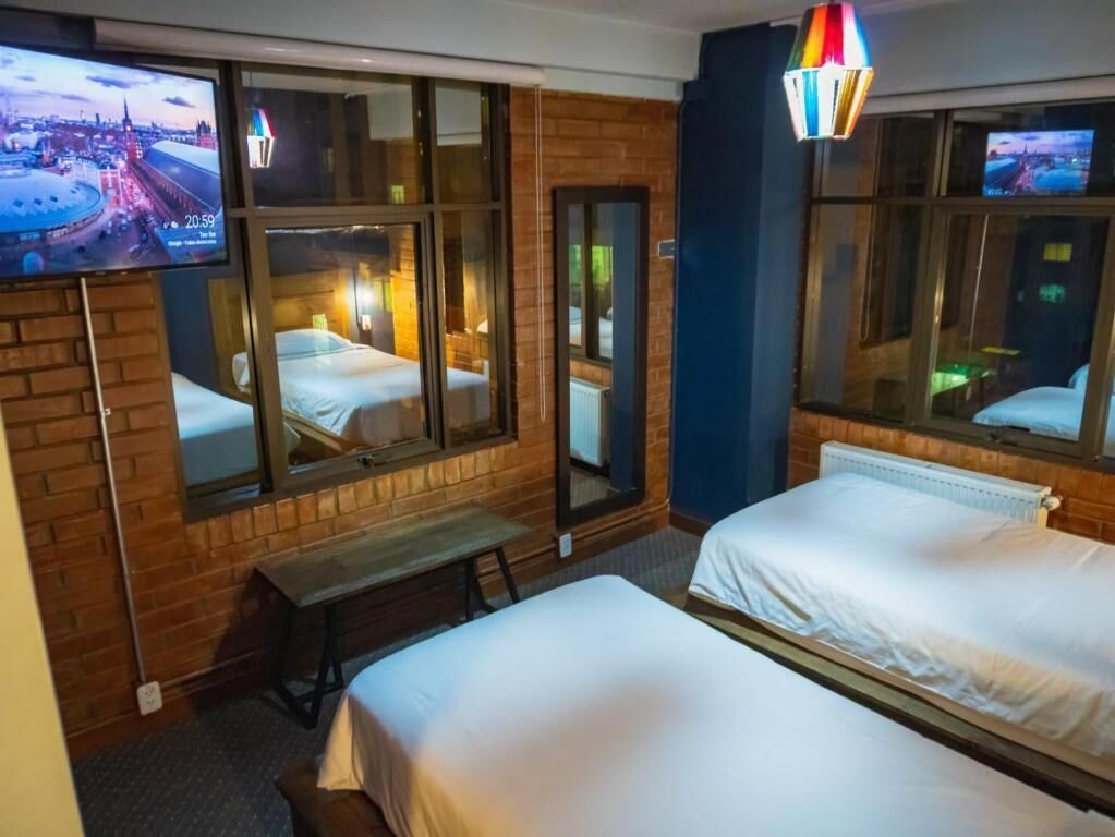 A hotel room with two beds, a bench, a TV, and a large window with a view of a cityscape.