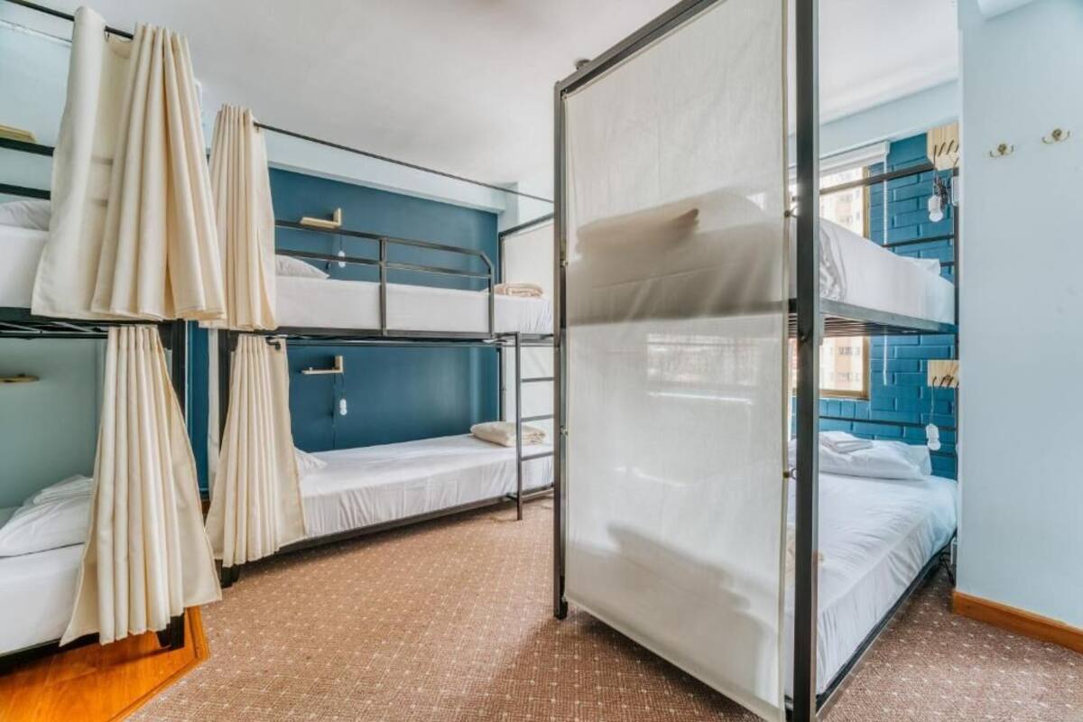 A dormitory room with bunk beds, a curtain, a sliding door, and a blue brick wall.