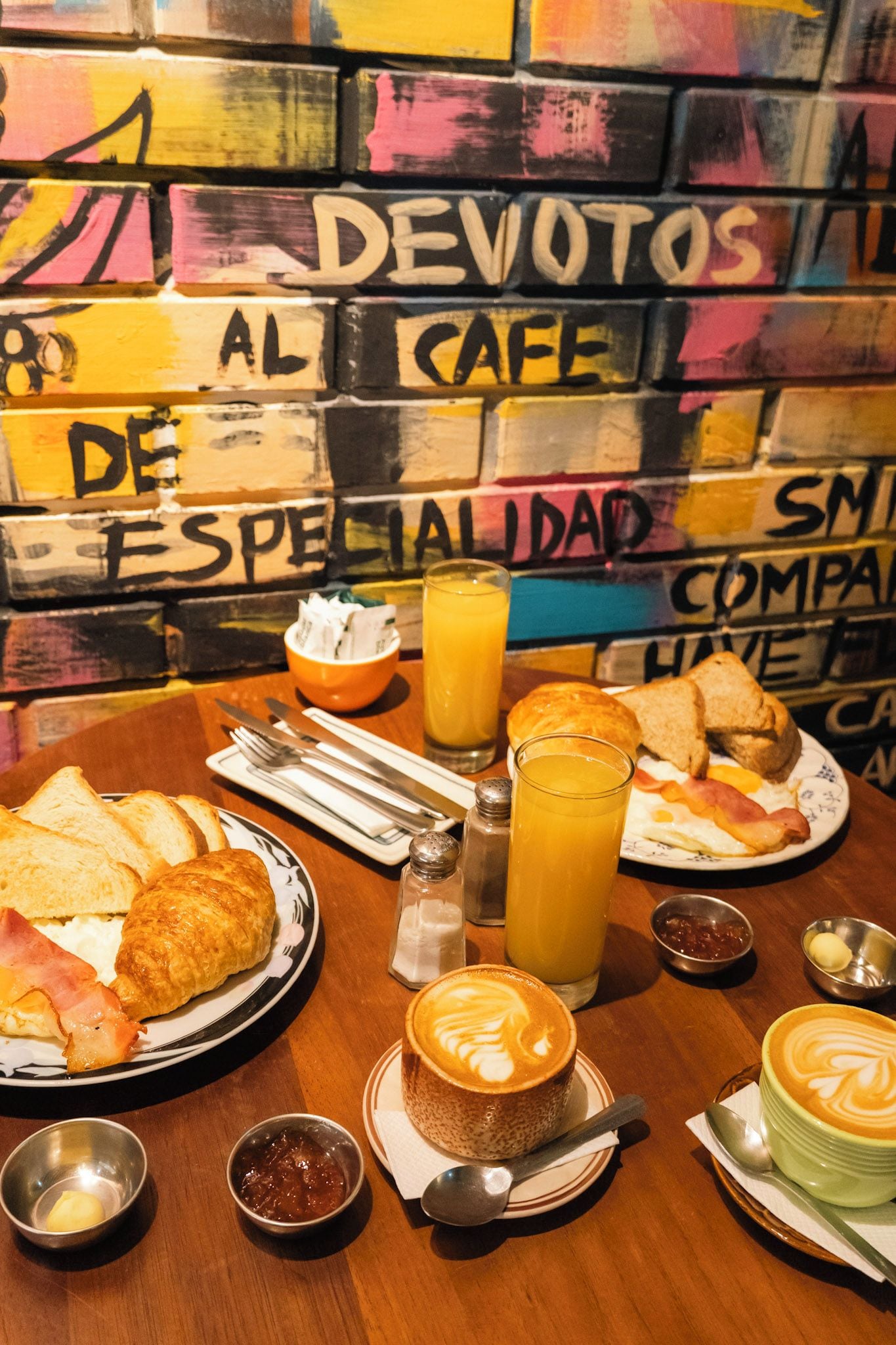 A breakfast setting with a variety of food items and a colorful graffiti wall in the background.