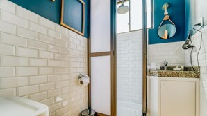 Une salle de bain avec des murs recouverts de carreaux blancs, une douche avec une porte en verre, des toilettes et un lavabo doté d’un plan de travail en granit.
