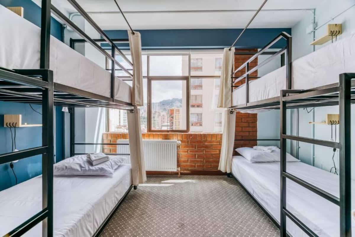 A dormitory room with bunk beds, a window with a view of buildings, and a radiator.