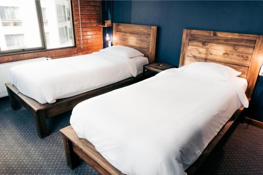 Two single beds with wooden headboards in a room with a brick wall and a window.