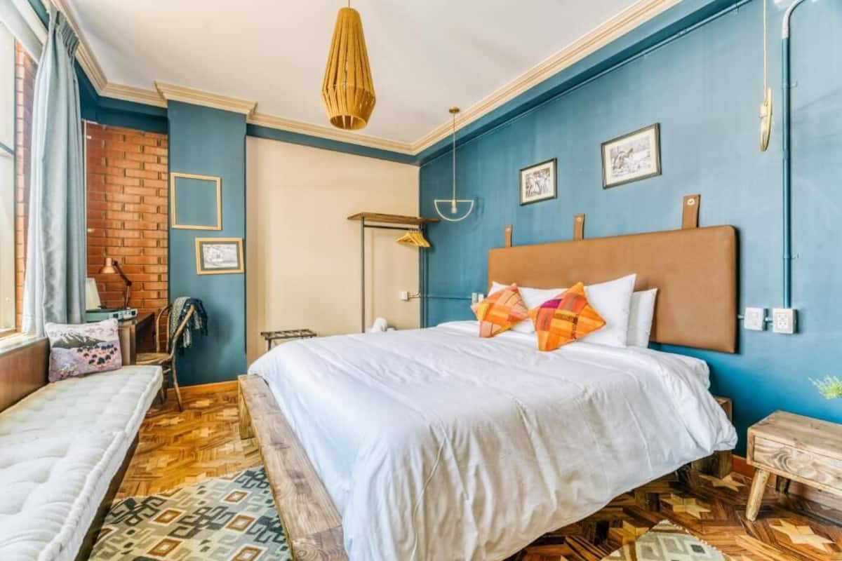 A bedroom with a large bed, a desk, a chair, and a hanging light fixture.
