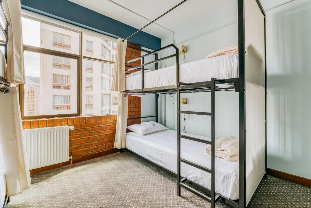 Une chambre avec un lit superposé, une fenêtre, un mur en briques et un radiateur.