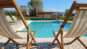 A poolside area with two wooden lounge chairs and a covered seating area.