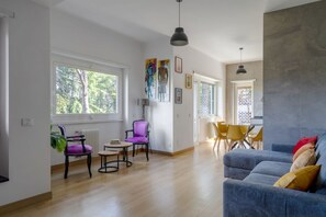 Ein geräumiger Wohnbereich mit einem blauen Sofa, einem Esstisch mit Stühlen und einem großen Fenster mit Blick auf Bäume.