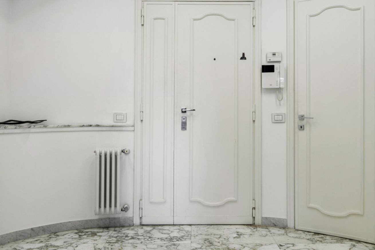 A white door with a handle, a thermostat, and a wall-mounted device.