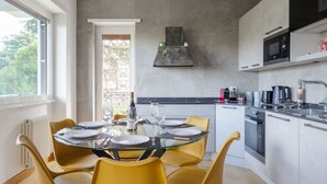 Et moderne køkken med spisebord til fire, indbygget ovn og et vindue med udsigt til grønne områder.