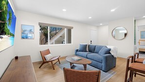 Ein modernes Wohnzimmer mit Sofa, Couchtisch und Sesseln, einer Treppe und einem großen Fenster mit Aussicht.