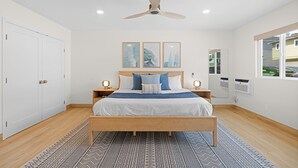 Ein Schlafzimmer mit einem Bett, Nachttischen, einem Deckenventilator, einem Fenster und einer Tür.