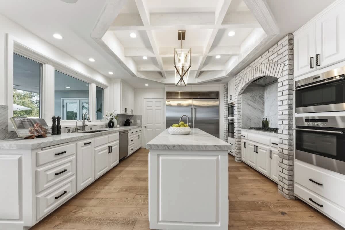 A modern kitchen with white cabinetry, a central island, a built-in oven, and a large window.