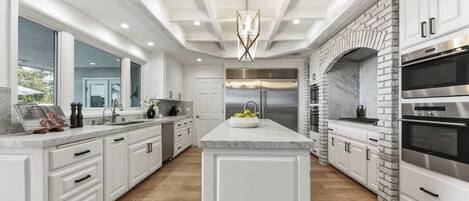 A modern kitchen with white cabinetry, a central island, a built-in oven, and a large window.