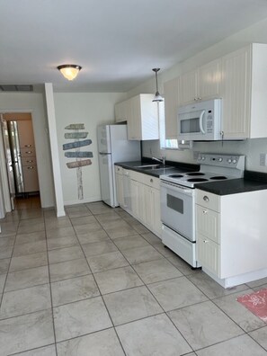A kitchen with white cabinets, a microwave, a stove, and a refrigerator. - WORK FROM HOME - LIVE IN PARADISE! 
Live on Sanibel Island - Walk to the beach! (Sanibel)