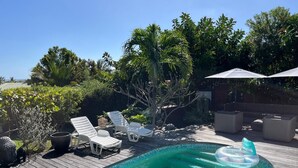 A wooden deck with a swimming pool, lounge chairs, and a floating ring. - Tropical villa - Orient Bay Park (Saint-Martin)