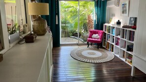 A room with a wooden floor, a round woven rug, a pink chair, a bookshelf, and a large window with curtains. - Tropical villa - Orient Bay Park (Saint-Martin)