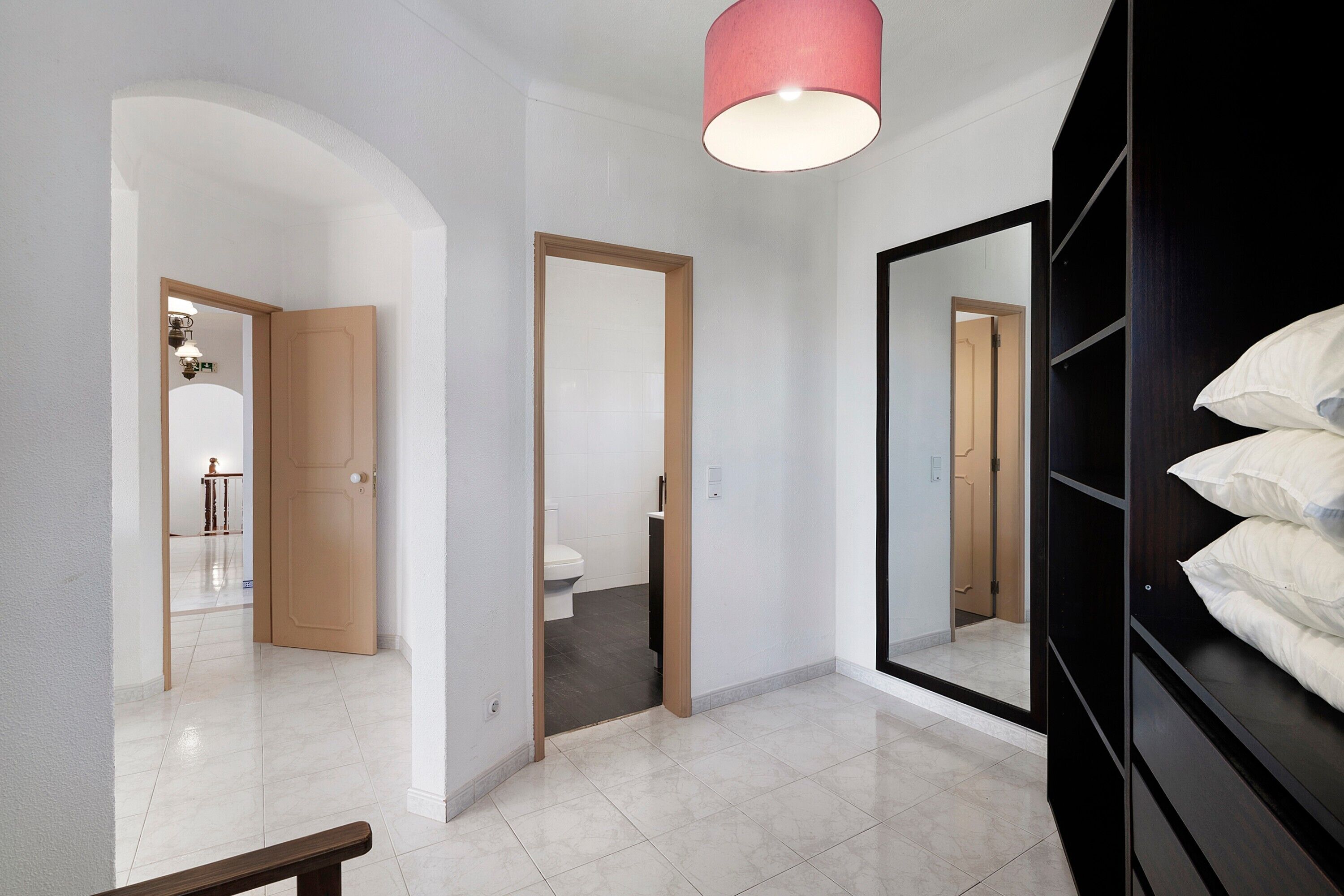 A hallway with a wooden door, a mirror, and a bed with white bedding.