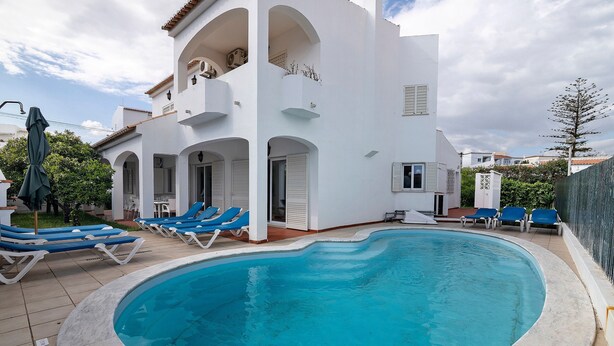 A swimming pool with lounge chairs, a white building with balconies, and a clear sky. - Villa Martins with Private Pool, Wi-Fi, and Air Conditioning (Albufeira)