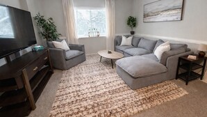 Een woonkamer met een televisie, twee banken, een salontafel en een vloerkleed.