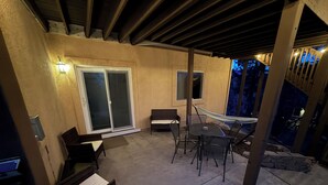Een terras buiten met een tafel, stoelen, een hangmat en een schuifdeur.