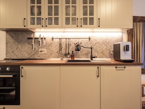 A kitchen with white cabinets, a stainless steel range hood, a water dispenser, and hanging utensils. - Cjase Longobarde (Cividale del Friuli)