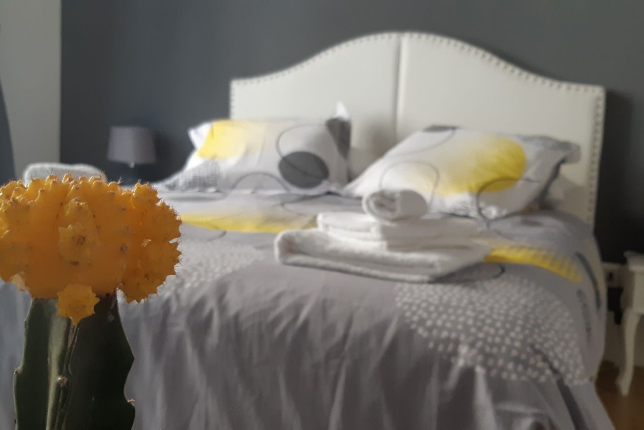 A bed with a white headboard, a grey and white patterned bedspread, and a yellow pillow.