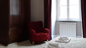 Ett sovrum med en stor säng, en röd stol, en trägarderob och ett fönster med gardiner.