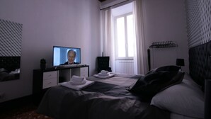 Ett hotellrum med en säng, en tv, ett skrivbord, en stol och ett fönster med gardiner.