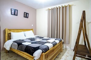 A wooden bed with a patterned bedspread, a wooden headboard, and a wooden chair. - Fantastic 2-bedroom apartment in the heart of Nyeri (Nyeri)